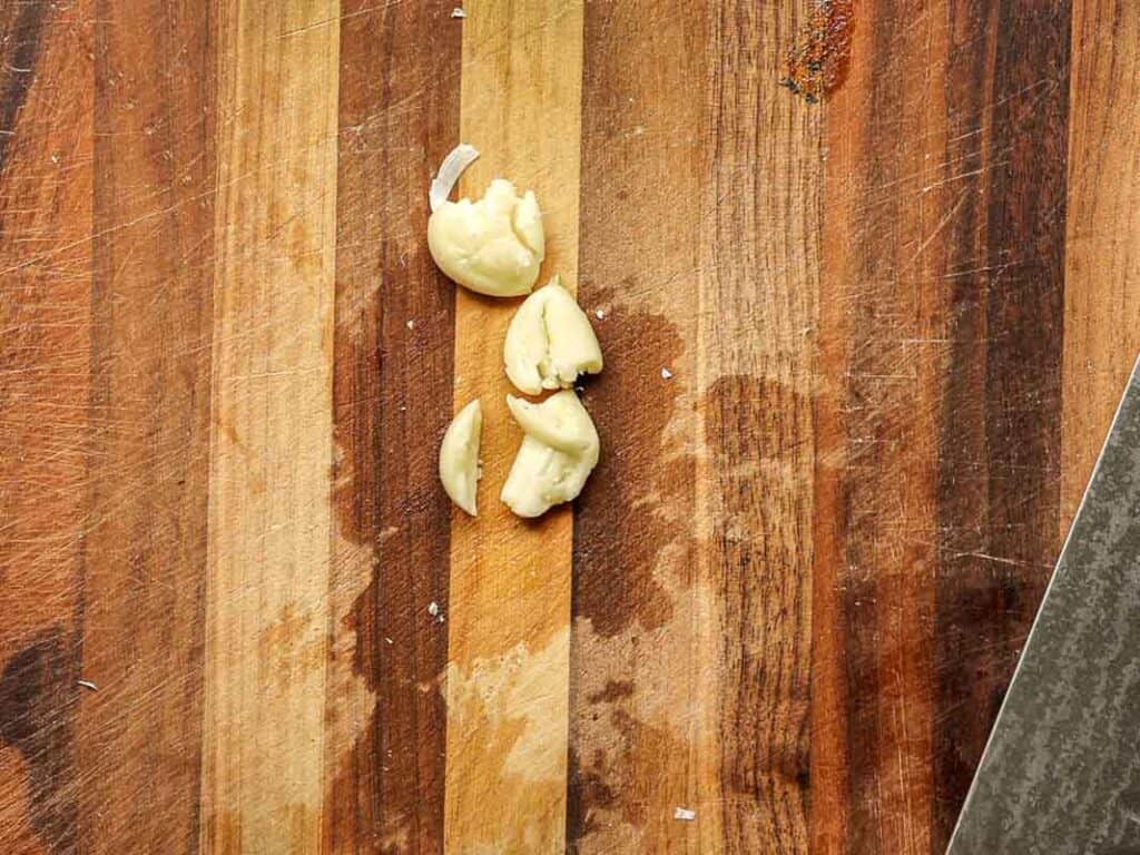 Chopped garlic cloves on a wooden cutting board with a knife visible on the side.